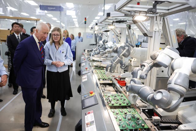 The King looks at robotic arms on a production line