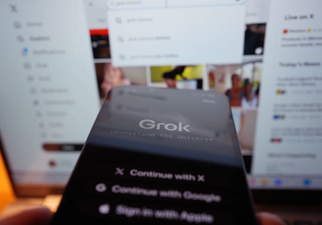 The Grok app on an iPhone, against the backdrop of search results displayed on the social media platform X (formerly Twitter) on a laptop