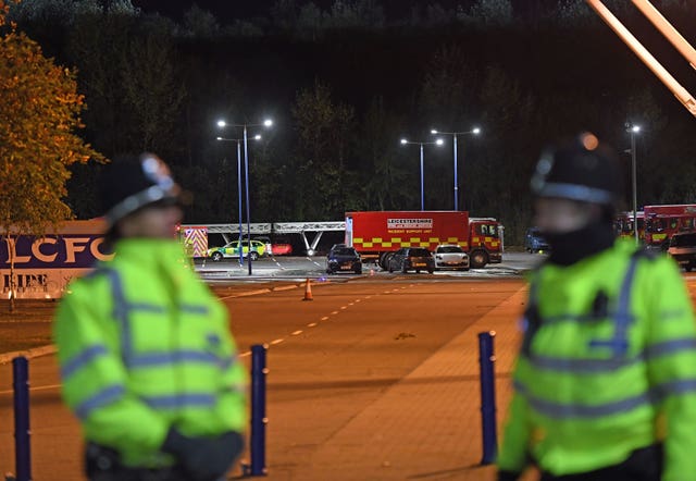 Two uniformed police officers in hi-vis are blurred in the foreground. In the background, recovery vans and cars are in focus