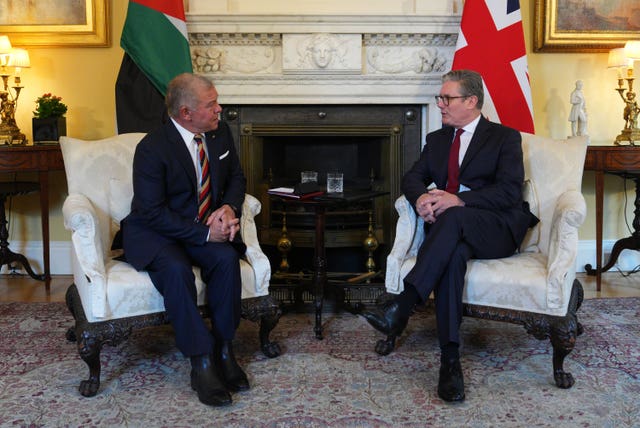 King Abdullah II and Keir Starmer on white chairs in front of an empty fireplace. The flags of the United Kingdom and Jordan are behind them