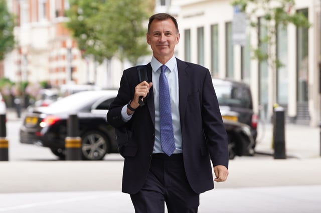 Jeremy Hunt in suit and tie, walking with a bag on his shoulder