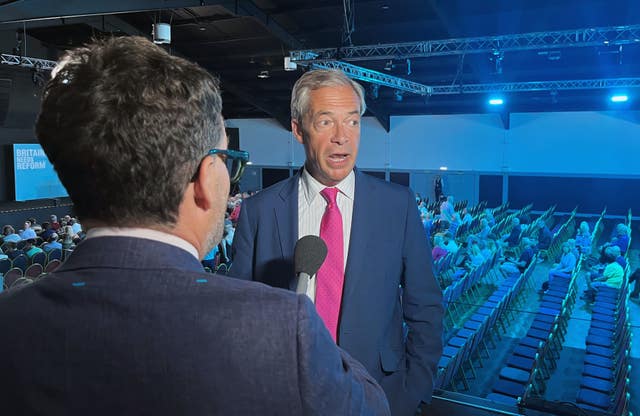Nigel Farage speaks to a reporter in front of a half-empty hall