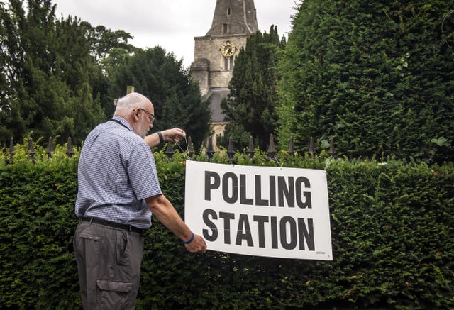 A man adjusts a polling station sign at Saint Martin Church in Womersley during voting for the Selby and Ainsty by-election in July 2023
