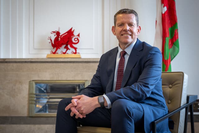 Rhun ap Iorwerth sitting in front of a Welsh flag