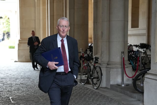 Secretary of State for Northern Ireland Hilary Benn holding a file and walking past stone pillars and bicycles