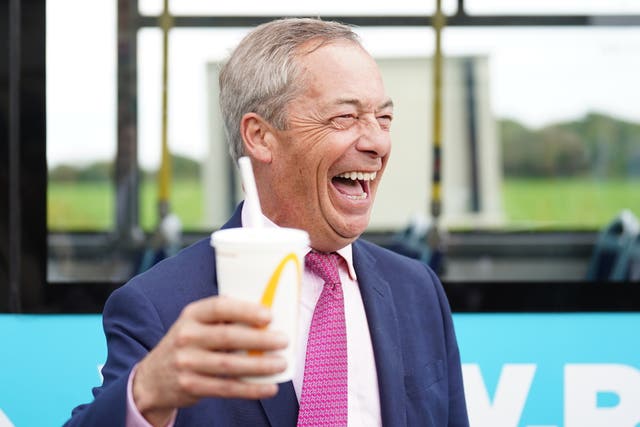 Nigel Farage grinning as he holds up a McDonald's milkshake cup 