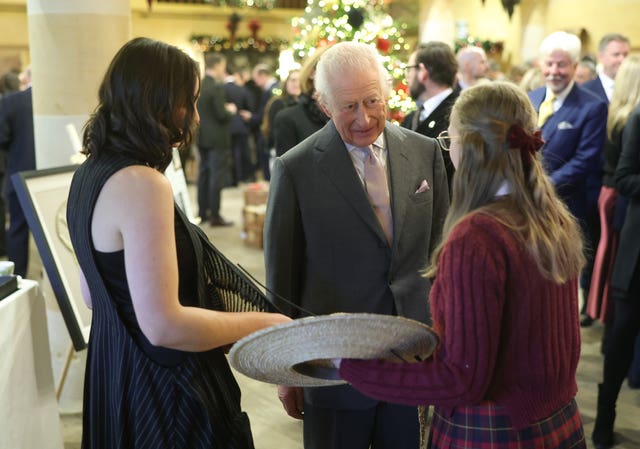 The King speaking to two young women showing him hats they created