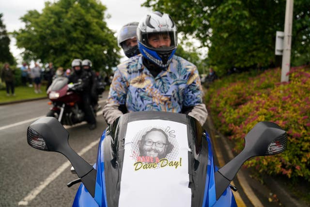 Two motorcyclists riding along a road with a picture of Dave Myers on the front of their bike