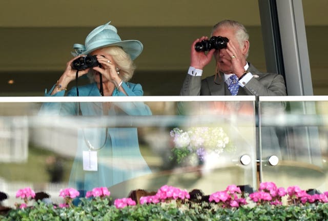 Charles and Camilla watch the King’s Stand Stakes through binoculars in the stands 