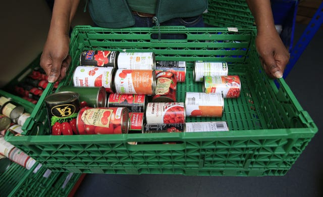 Closeup of two hands holding a tray of tinned cans and a food bank 