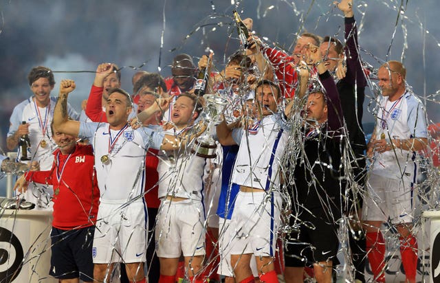 England’s Robbie Williams (centre left) lifts the trophy with Jonathan Wilkes (centre right) as they celebrate winning Soccer Aid 2016 at Old Trafford, Manchester (Nigel French/PA)