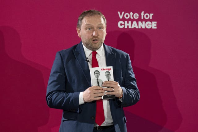 Ian Murray holding a copy of the Labour manifesto, with the words 'Vote for change' behind him
