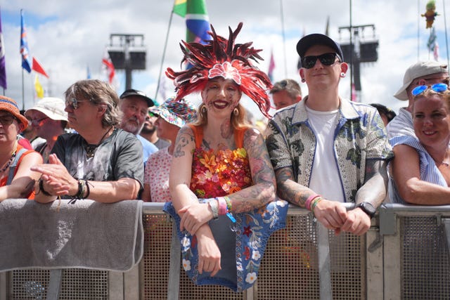 Fans at the front of the stage including a woman wearing a feathered headdress and a top covered in orange flowers