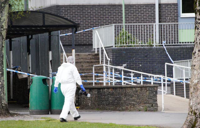 A forensic investigator in white overalls outside a school building