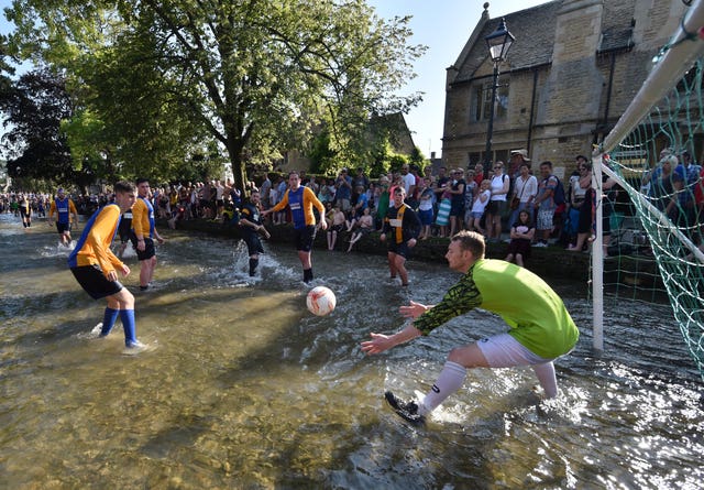 Bourton Rovers 1st team (yellow sleeves) and Bourton Rovers 2nd team (in solid blue) play each other in the annual traditional river football match in the Cotswolds village of Bourton-in-the-Water