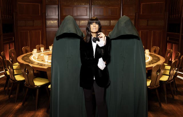 Claudia Winkleman standing between two hooded figures