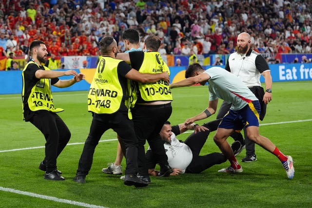 A security guard slips and collides with Spain’s Alvaro Morata, second right, as a pitch invader is accosted after the match