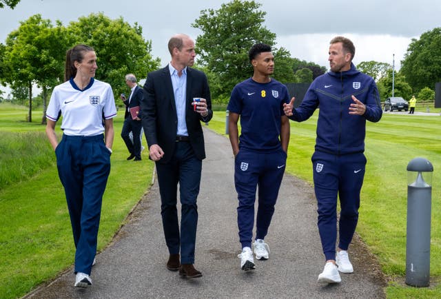 From left, Jill Scott, the Prince of Wales, Ollie Watkins and Harry Kane waking in a row along a path at St George’s Park