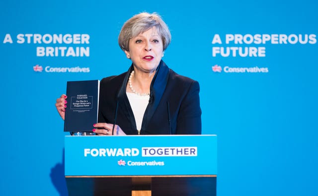 Theresa May behind a podium holding a copy of the Conservatives' 2017 election manifesto