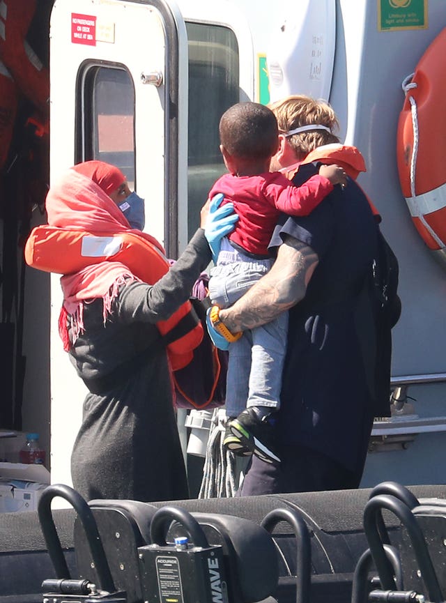 A Border Force officer helps a young boy comforted by his mother from a Border Force vessel