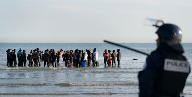 A French police officer watches people preparing to board a small boat in the Channel