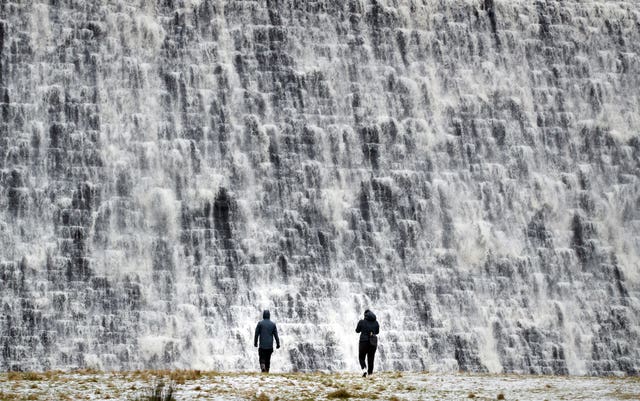 People watch as water cascades down Derwent Dam in the Peak District