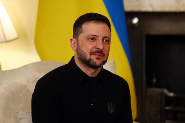 Volodymyr Zelensky seated in front of a Ukrainian flag