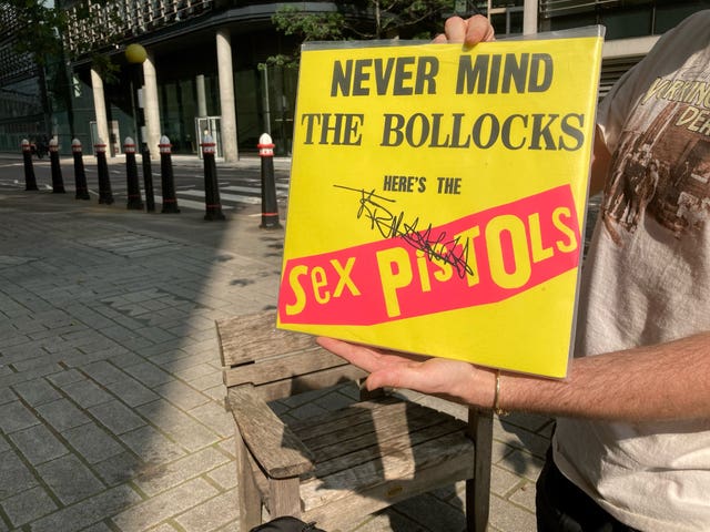 A member of the public holds a copy of the Sex Pistols’ Never Mind The Bollocks, signed by John Lydon, outside the court 