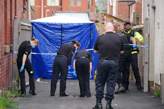 A blue tent in an alleyway with a number of police officers in all-black searching around the floor