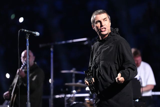Liam Gallagher on stage wearing a black jacket standing in front of a microphone