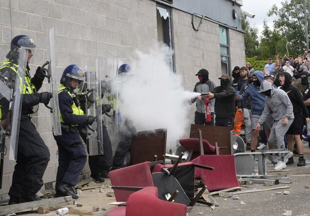 An individual at the front of a group of people sprays the contents of a fire extinguisher at police officers behind riot shields outside a hotel in Rotherham