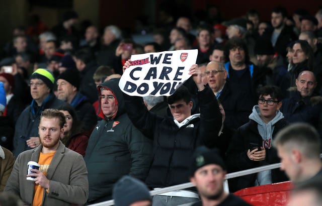 An Arsenal fan holds up a 'We care, do you?' banner