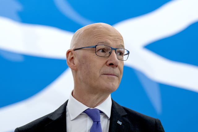 John Swinney looking off-camera, in front of a Saltire flag