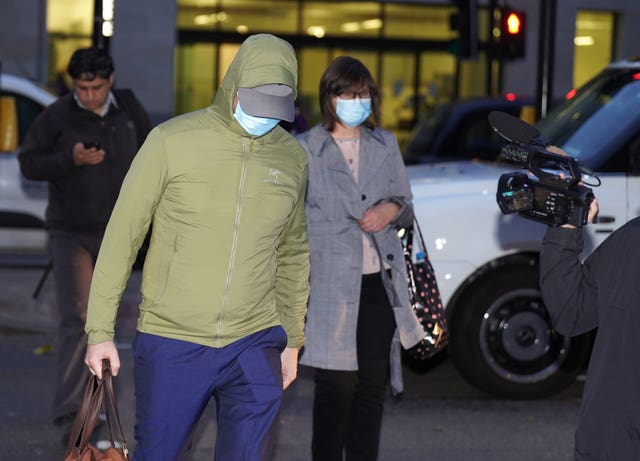 Joel Borders leaving Westminster Magistrates' Court wearing green jacket and medical mask and carrying holdall alongside woman in medical mask