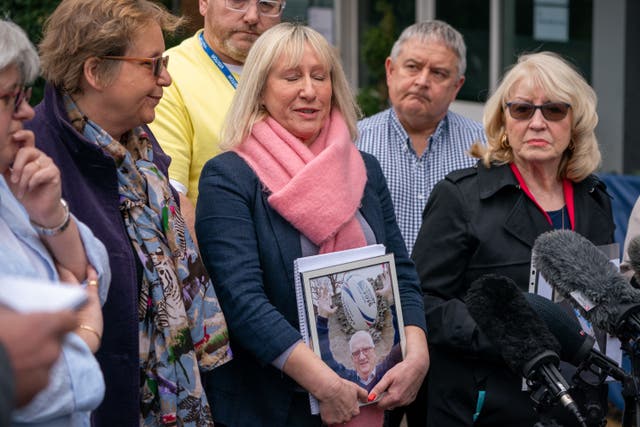 A woman in a pink scarf holds a picture of a loved one as she speaks about the pandemic 