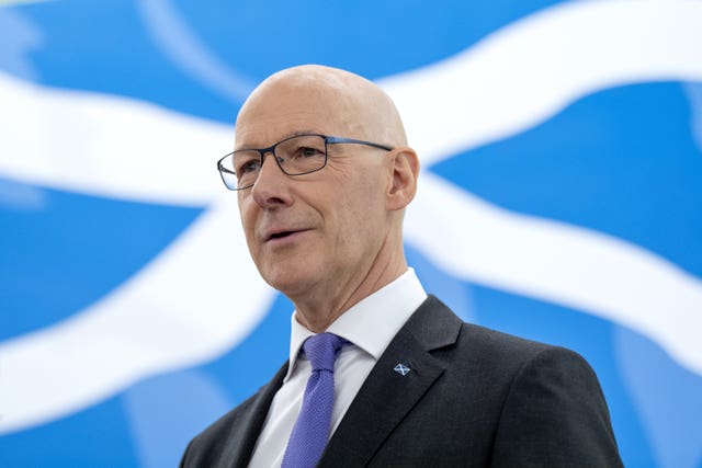 First Minister John Swinney speaks with a saltire flag as a background