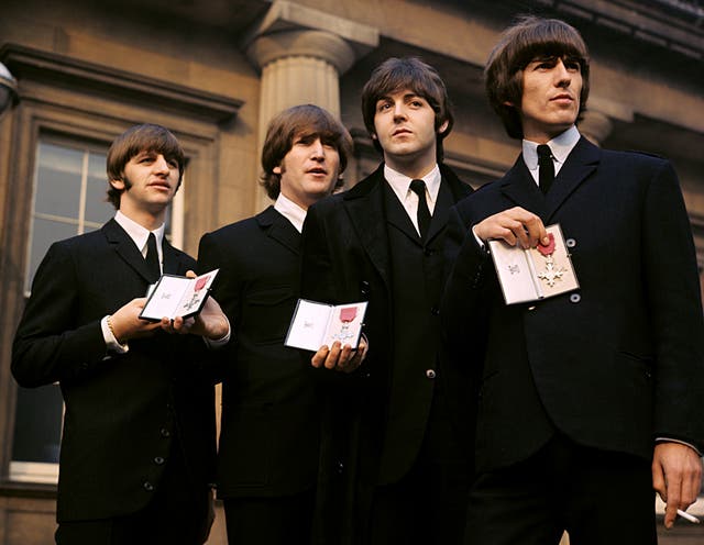 The Beatles showing their MBE Insignias in the forecourt after receiving them from the Queen (PA)