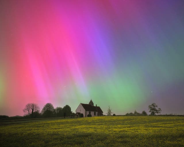 Red, green and purple aurora lights over a field with a white church 