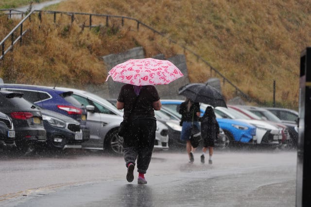 Beachgoers shelter from the rain under umbrellas 