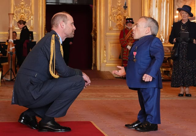 The Prince of Wales, left, crouching down to be at eye level with Warwick Davis during an investiture ceremony at Windsor Castle