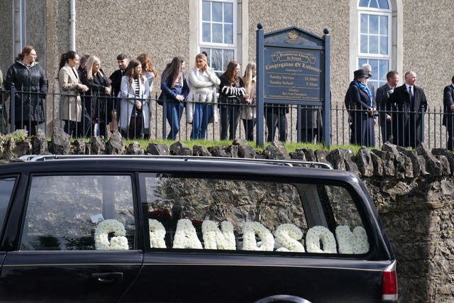 Mourners and a hearse with floral tributes outside Lislooney Presbyterian Church