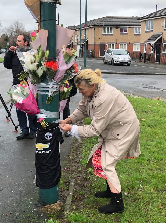 A woman ties a tribute of flowers to a lamppost 