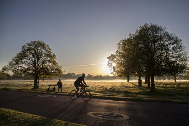 A cyclist in silhouette riding a bicycle in between two trees as the sun rises in Richmond Park on an April morning