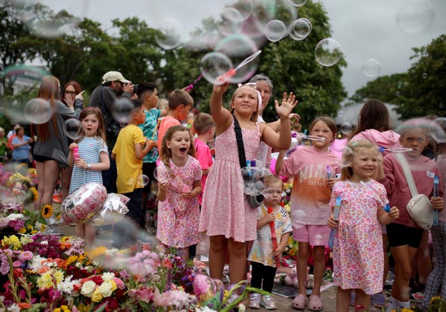 Young children play with bubble wands among floral tributes