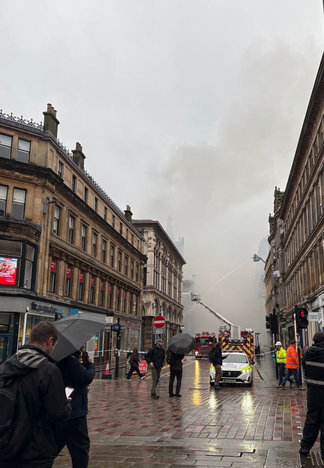 People look at smoke rising as firefighters damp down the remains of the fire