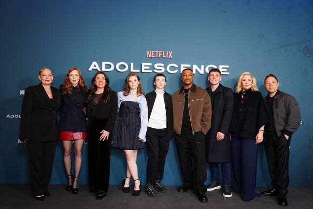 Adolescence cast standing in a row, in front of signage publicising the show