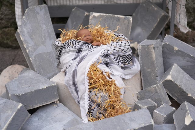 A doll representing the baby Jesus lies on hay wrapped in a Palestinian scarf on blocks of concrete 