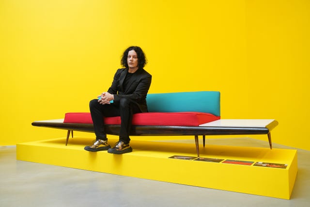 Jack White sitting on a sofa on a yellow plinth with a yellow background