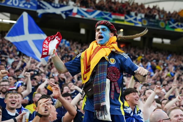 A Scotland fan with face paint stands in front of fellow supporters at the Euro 2024 match against Hungary