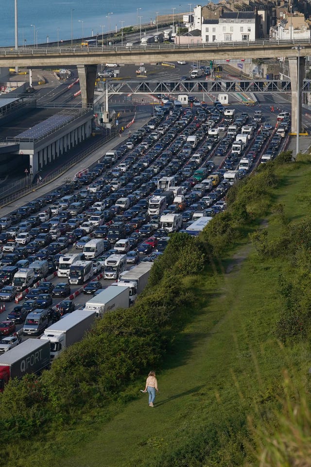 A woman walks across the cliffs while holiday and freight traffic queue to use the Port of Dover